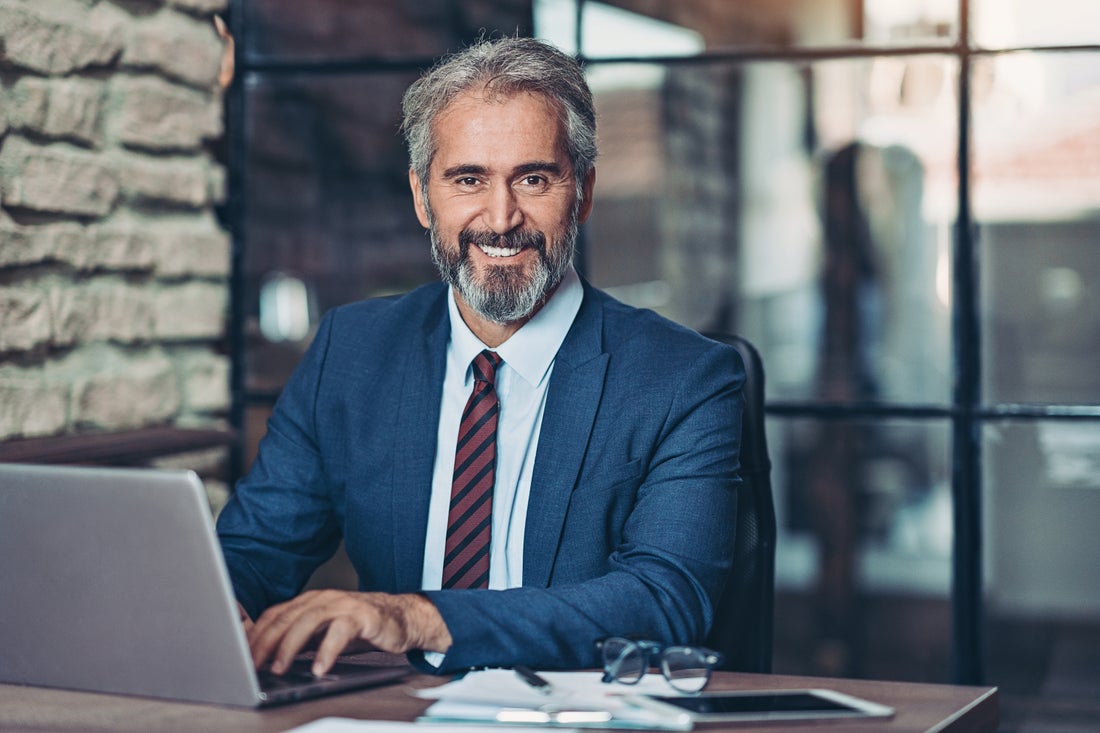 a man wearing a suit and tie sitting in front of a laptop