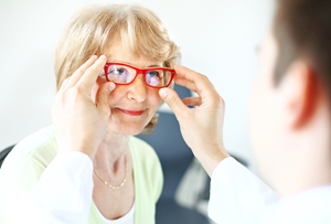 eye doctor putting red glasses on elderly woman